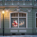 Weihnachtsmann mit Schlitten und Rentieren als Hologramm im Sprossenfenster eines verschneiten Altbaus